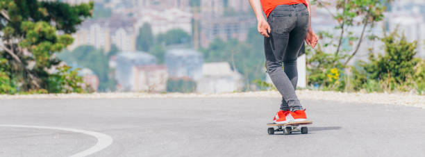 großer athlet fährt mit seinem longboard schnell und stetig bergab, während er rotes t-shirt und schwarze jeans trägt. - longboard skating stock-fotos und bilder