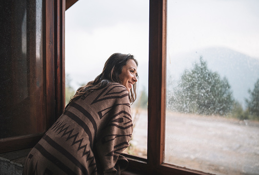 Woman on the window of a log cabin enjoying the beautiful rainy day in nature