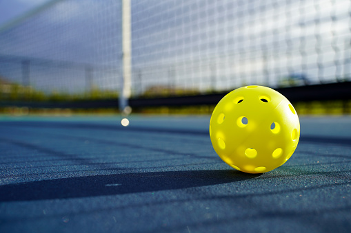 Pickleball on court with net in background.