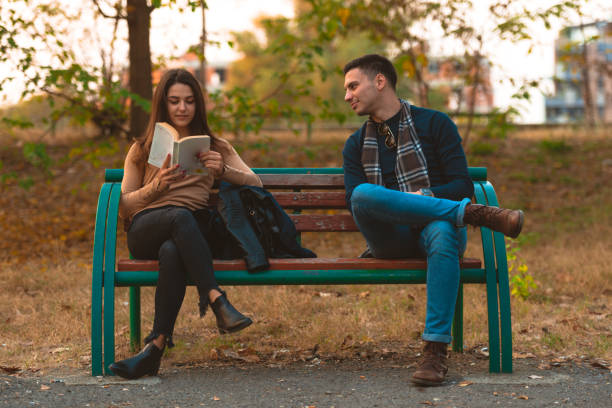 istock A beautiful girl is reading a book while handsome man is trying to get her attention. 1361641082
