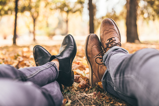 Legs of a guy and a girl resting in the park, showing black and brown shoes
