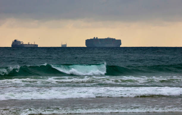 istock Group of container ships waiting offshore with a wave breaking in the foreground 1361660272