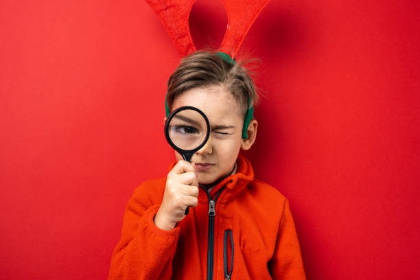 one boy in front of red background wall holding lens magnifying glass looking to the camera copy space front view waist up - magnifying glass lens holding europe imagens e fotografias de stock