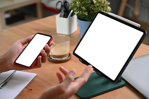 Close up view man holding smart phone and using computer tablet.