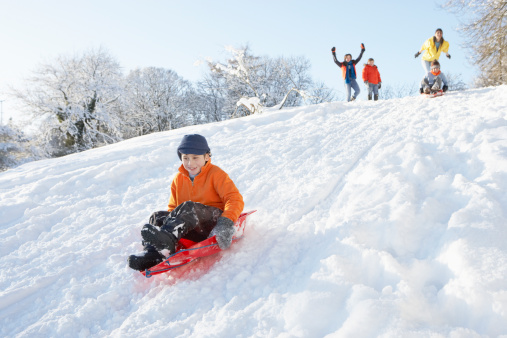 Young Boy Sledging Down Hill With Family Watching And Cheering