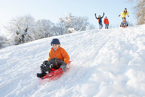 Young Boy Sledging Down Hill With Family Watching stock photo