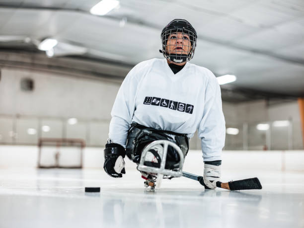 Mature Disabled Latin woman playing sledge hockey Mature Disabled Latin woman practising sledge hockey. She is wearing full sledge hockey gear with jersey featuring her own print with universal symbols of various disabilities. She is also wearing full protection hockey helmet with face mask. Interior of hockey rink. adaptive athlete stock pictures, royalty-free photos & images