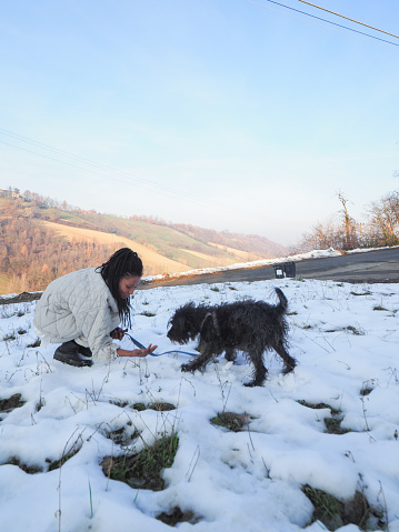 young african woman enjoying winter weather in the mountains playing with her pet puppy black terrier dog in the snow a sunny cold  day