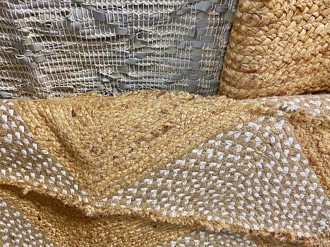 Horizontal close up of textured material hand woven into throw rug carpets and mats in neutral beige tan and grey color tones creates abstract background design