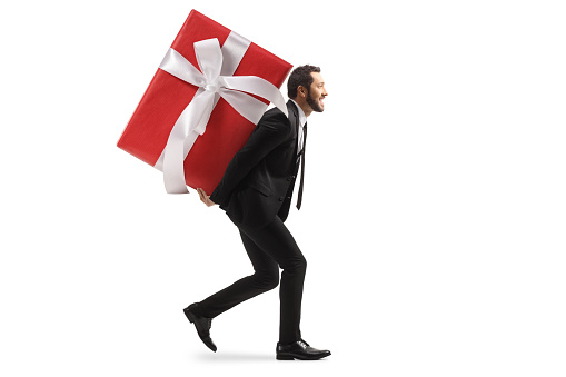 Full length profile shot of a businessman carrying a big wrapped present on his back isolated on white background