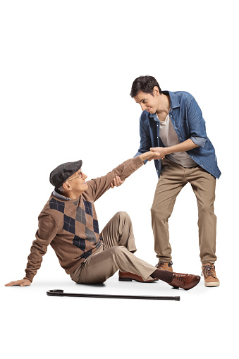 Young man helping an elderly man with a cane seated on the floor isolated on white background