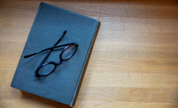 hardcover notebook on a table. closed old black book and eyeglasses on wooden background, top view - book school desk old imagens e fotografias de stock