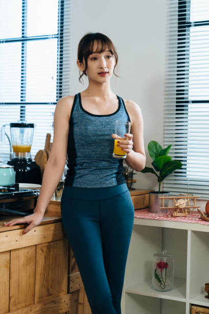istock vertical shot asian athletic female is standing with elegance and looking into distance while having fresh juice on a tranquil morning after training at home. 1361687368