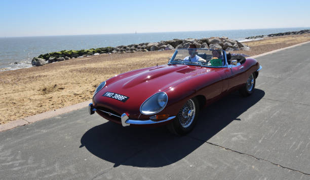 voiture décapotable jaguar jaguar e type rouge classique conduite le long de la promenade du front de mer. - e type photos et images de collection