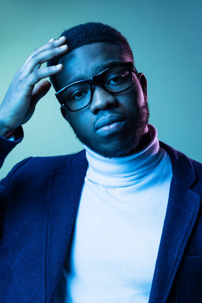 retrato de close-up de jovem homem africano elegante, estudante vestindo pescoço-polo branco e jaqueta isolada em fundo azul em luz de neon. - polo shirt african ethnicity men african descent - fotografias e filmes do acervo