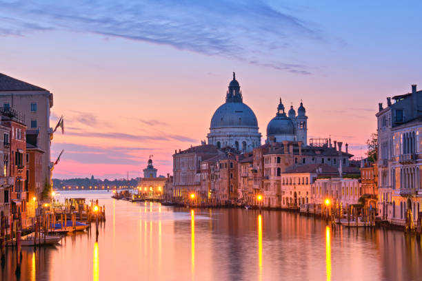 Romantic Venice at dawn, sunrise. Cityscape image of Grand Canal in Venice, with Santa Maria della Salute Basilica reflected in calm sea Romantic Venice at dawn, sunrise. Cityscape image of Grand Canal in Venice, with Santa Maria della Salute Basilica reflected in calm sea. Street lights reflected in calm water. venice italy stock pictures, royalty-free photos & images