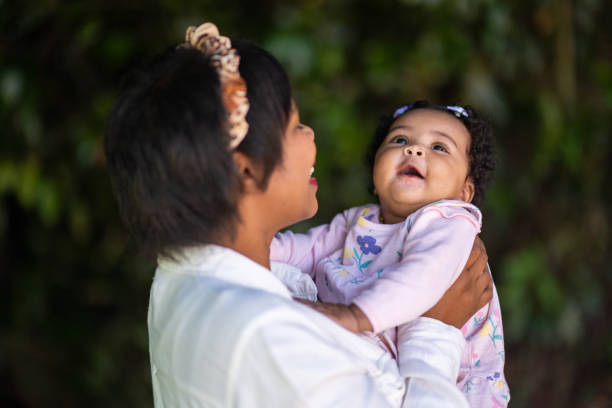 istock Young mother holding cute young baby looking up smiling outdoors having fun 1361708870