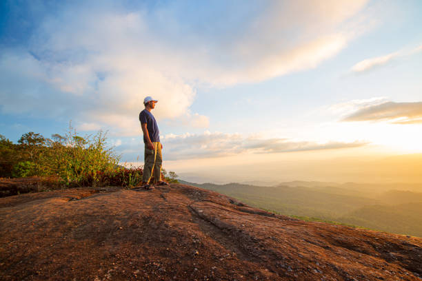 istock Young man with backpack standing with raised hands on top of a mountain and enjoying valley view 1361709459