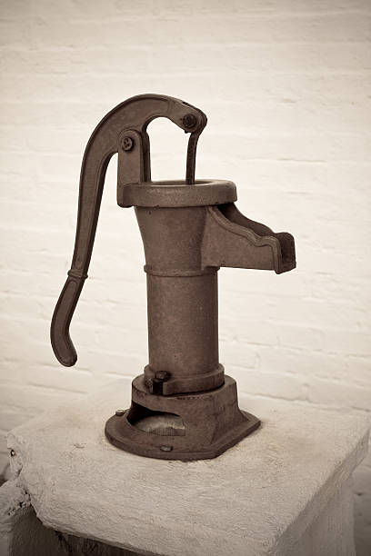 handle and spout of old, rusty hand water pump against white brick wall, with vignetting