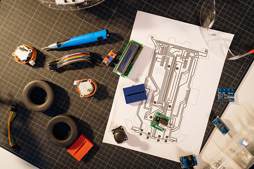 Blueprint with the construction of a robotic car, electrical equipment, and work tools on the table at the home workshop