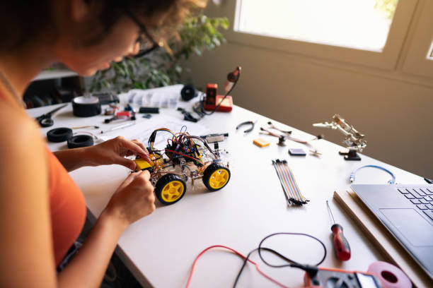 istock Female robotic engineering student, connecting cables of the autonomous self-driving robotic car with sensors with mother board in her creative home workshop 1361713655