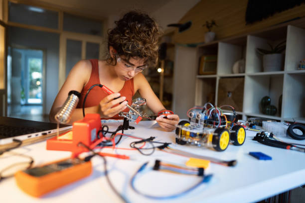 istock Focused female robotic engineering student, soldering metal wire for a construction part with soldering iron, while making robotic car 1361714963