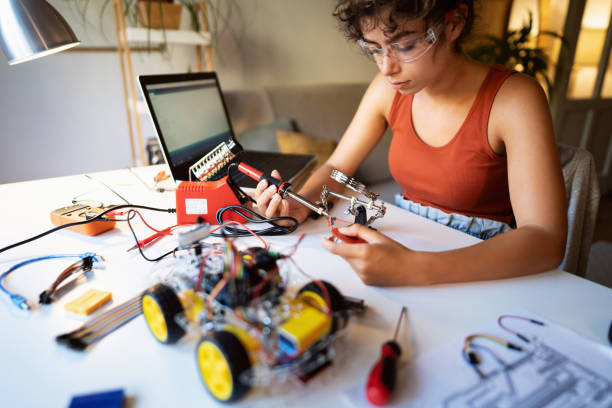 istock Female engineering student, soldering metal wire for a construction part with soldering iron, while making robotic car 1361715117