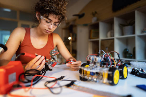 istock Female robotic engineer using magnifier, while connecting the wire to construction part of robotic car with soldering iron 1361715150