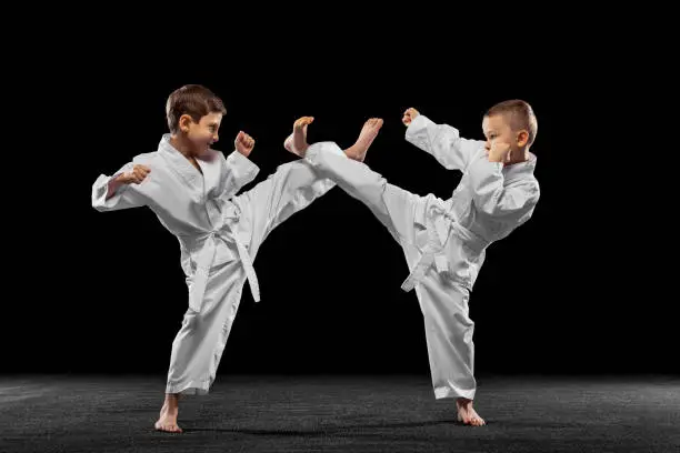 Sparring. Two little kids, boys, taekwondo athletes training together isolated over dark background. Concept of sport, education, skills, workout, healthy lifestyle and ad. Power and energy.