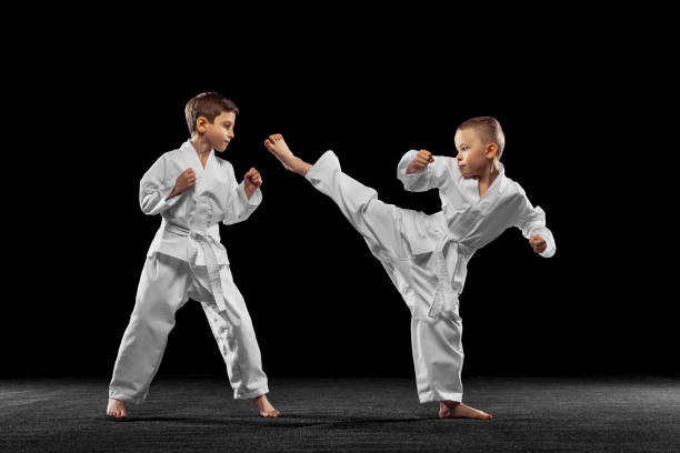 dos niños pequeños, niños, atletas de taekwondo entrenando juntos aislados sobre un fondo oscuro. concepto de deporte, educación, habilidades - taekwondo fotografías e imágenes de stock