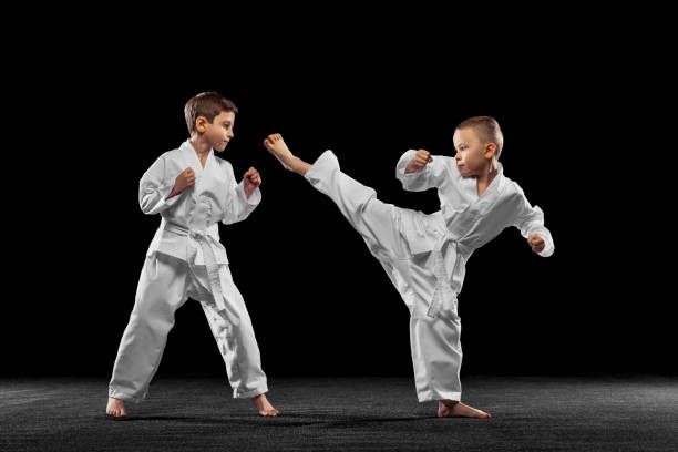 due bambini piccoli, ragazzi, atleti di taekwondo che si allenano insieme isolati su sfondo scuro. concetto di sport, educazione, competenze - tae kwon do foto e immagini stock