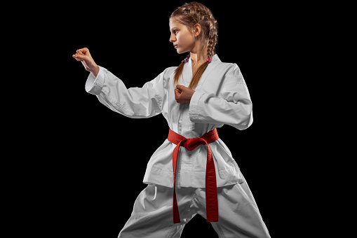 Punch. One young girl, teen, taekwondo athlete posing isolated over dark background. Concept of sport, education, skills, workout, healthy lifestyle and ad. Power and energy.