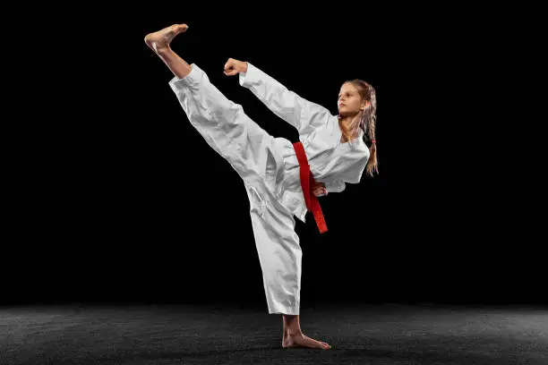Leg kick. Portrait of young girl, teen, taekwondo athlete practicing alone isolated over dark background. Concept of sport, education, skills, workout, healthy lifestyle and ad. Power and energy.
