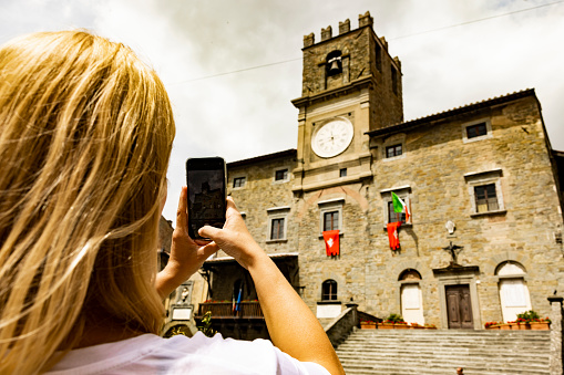 View of a woman talking souvenir photos with a smartphone in a small town, Tuscany, Italy.