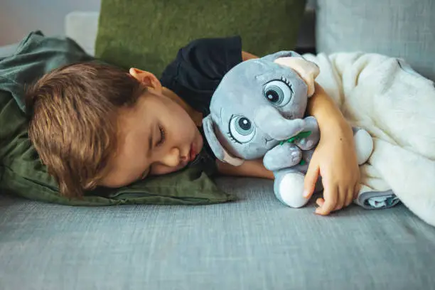Boy sleeping on bed with elephant toy green pillow and sheets. Boy fall asleep in morning. Sleep concept. Adorable kid boy after sleeping in bed with toy. Sleepyhead