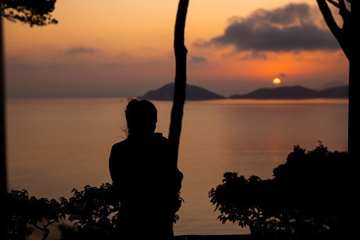 View of a woman looking the Mediterranean Sea at sunset along the coast on Elba Island, Italy.