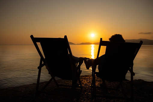 View of a couple sitting on beach chairs along the coast at sunset looking the sea, Elba Island, Italy.