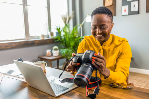 Happy young photographer holding a dslr camera Happy young photographer holding a dslr camera in her home office. Female photographer smiling cheerfully while working at her desk. Creative female freelancer working on a new project. creative space photos stock pictures, royalty-free photos & images