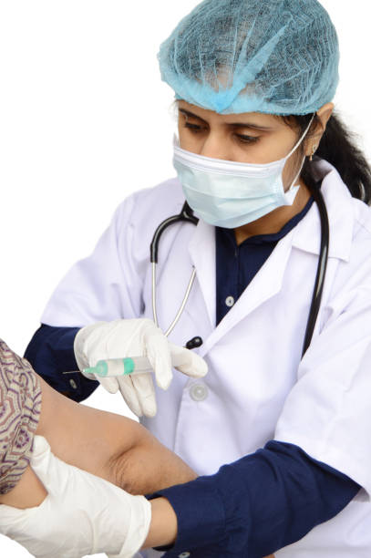 外科マスク、キャップ、白いラボコートを着た女性または女性医師が、注射器針注射を手に首の周りの聴診器を持ち、テキスト用のコピースペースを持つ白い背景の上に隔離された患者に用� - syringe medical injection surgical needle surgical mask ストックフォトと画像