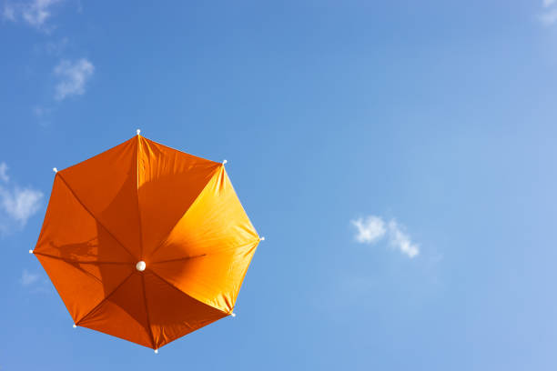 A close-up view from the low, a beautiful, translucent orange umbrella floating freely in the blue sky in the springtime sunlight of the Thai countryside.