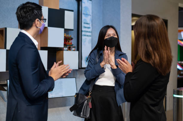 asian chinese colleague back to work with protective face mask greeting other colleagues at office entrance in the morning - cheering business three people teamwork imagens e fotografias de stock