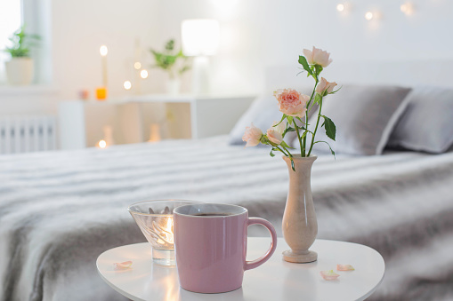 pink cup of coffee and  roses  in vase on table in bedroom