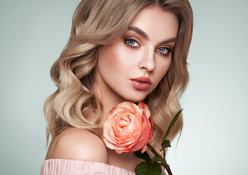 A beautiful young woman with shiny wavy blonde hair. Model with healthy skin, close up portrait. Girl with a rose flower