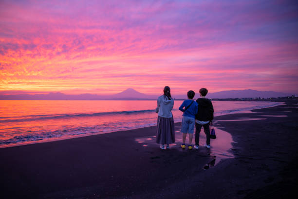 rückansicht von drei personen, die den berg fuji vom shonan beach bei sonnenuntergang betrachten - chubu region stock-fotos und bilder