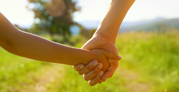 Close-up of mother and daughter holding hands while walking in the field.