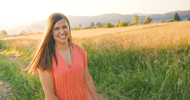 Happy mid adult woman on meadow Portrait of smiling mid adult woman walking on meadow in the field. peach color dresses stock pictures, royalty-free photos & images