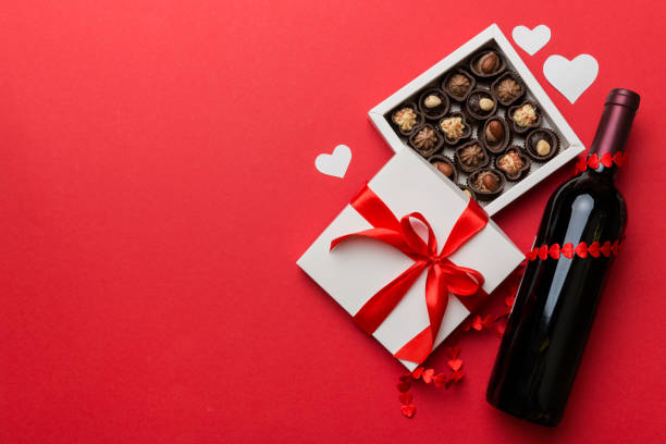 bouteille de vin rouge sur fond coloré pour la saint-valentin avec cadeau et chocolat. en forme de cœur avec boîte cadeau de chocolats vue du dessus avec espace de copie - heart shape stone red ecard photos et images de collection