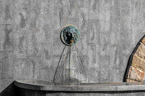 A jet of water flows from the mouth of a lion head on a granite wall. An old facade faucet-fountain on the Cascade Staircase in Shevchenko garden in Kharkiv, Ukraine