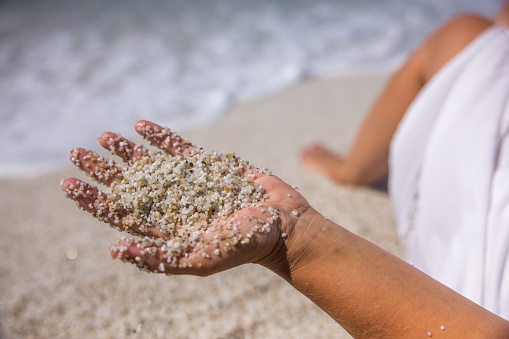 View of woman's hand playing with sand along the beach in Sardinia, Italy.