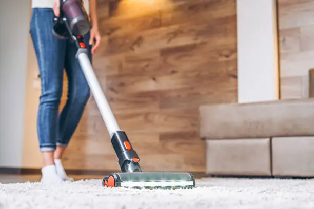 Photo of oman cleaning floor and carpet with cordless vacuum cleaner at home.